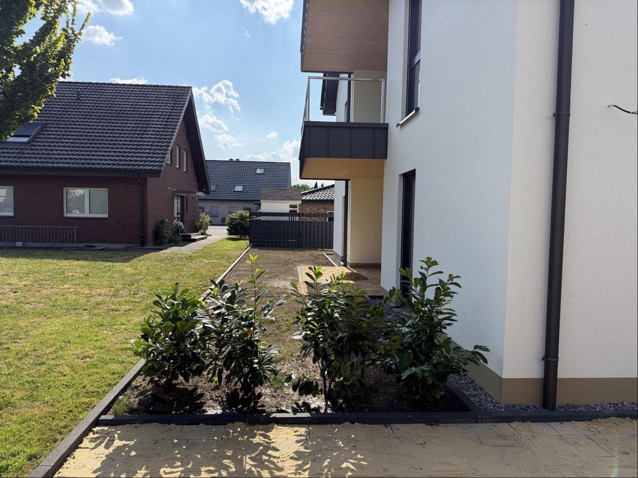 Neu gepflasterter Weg mit frisch angelegter Randbepflanzung neben einem Neubau